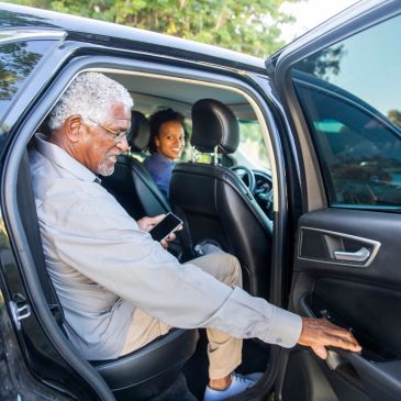 Elderly man opening car door while a woman sits inside.