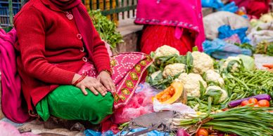 Woman in traditional attire selling fresh vegetables at an outdoor market.