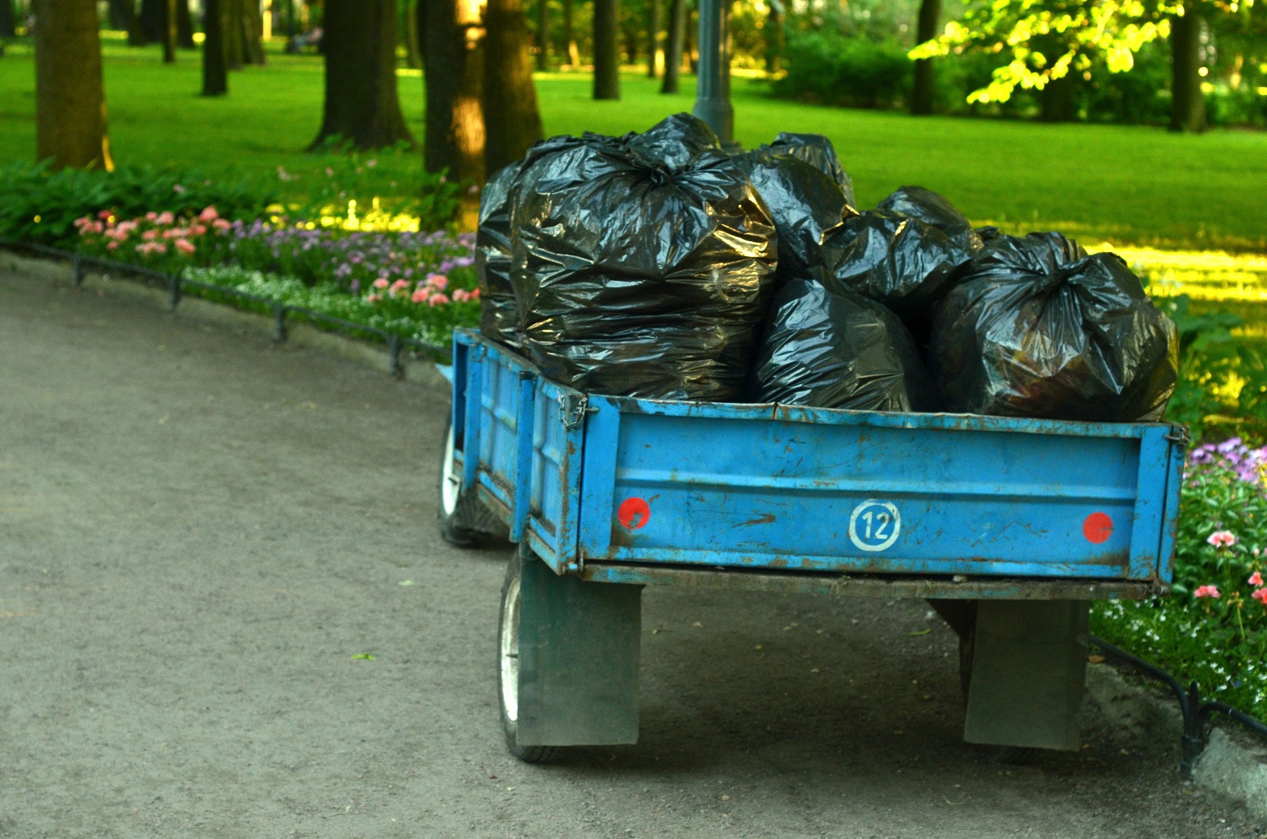 A blue cart filled with black garbage bags in a park.