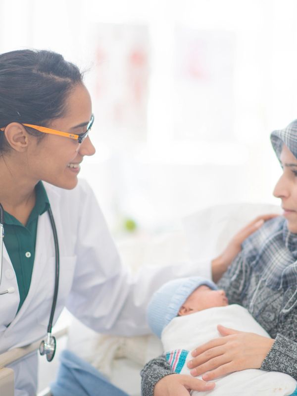 Doctor comforting a new mother holding her baby in a clinical setting.