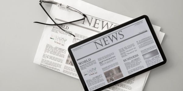 Tablet displaying news on top of a newspaper with glasses.