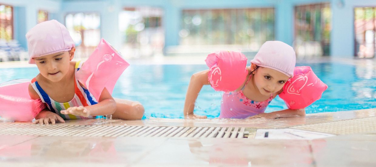 An elderly woman teaches a baby to swim in a pool.