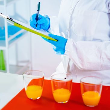 Scientist in protective gear documents data with orange liquid samples.
