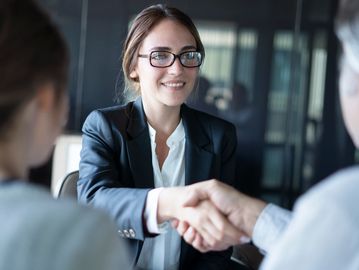 Businesswoman shaking hands with a client in an office setting.