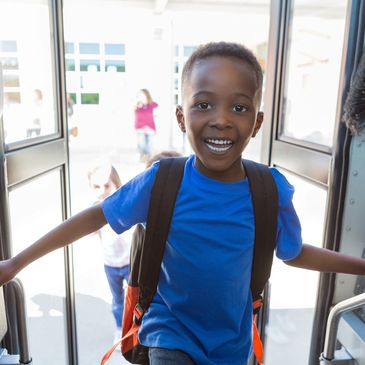 Smiling boy with a backpack boarding a school bus.