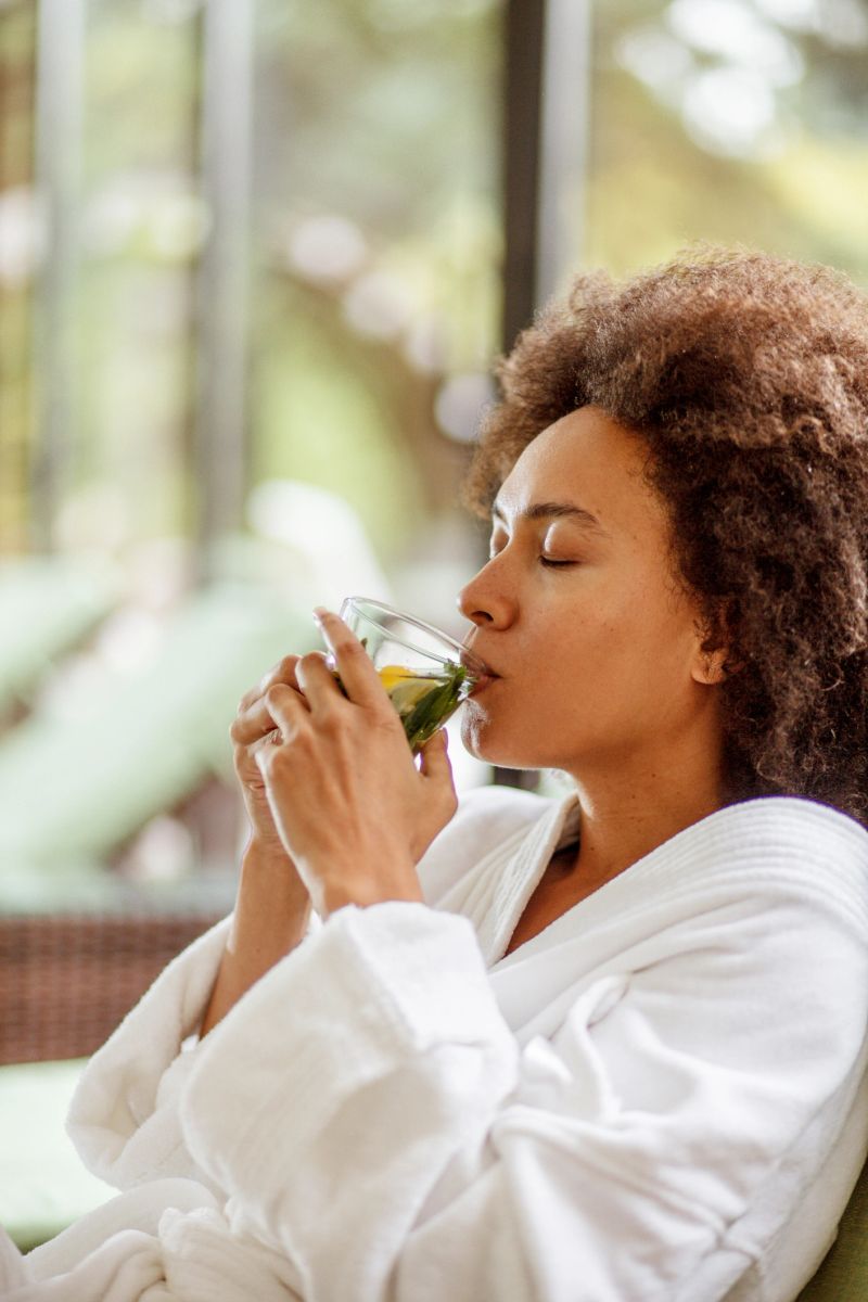 Beautiful mixed race young woman drinking a refreshing cup of herbal tea while relaxing in a cozy bathrobe at the wellness resort.