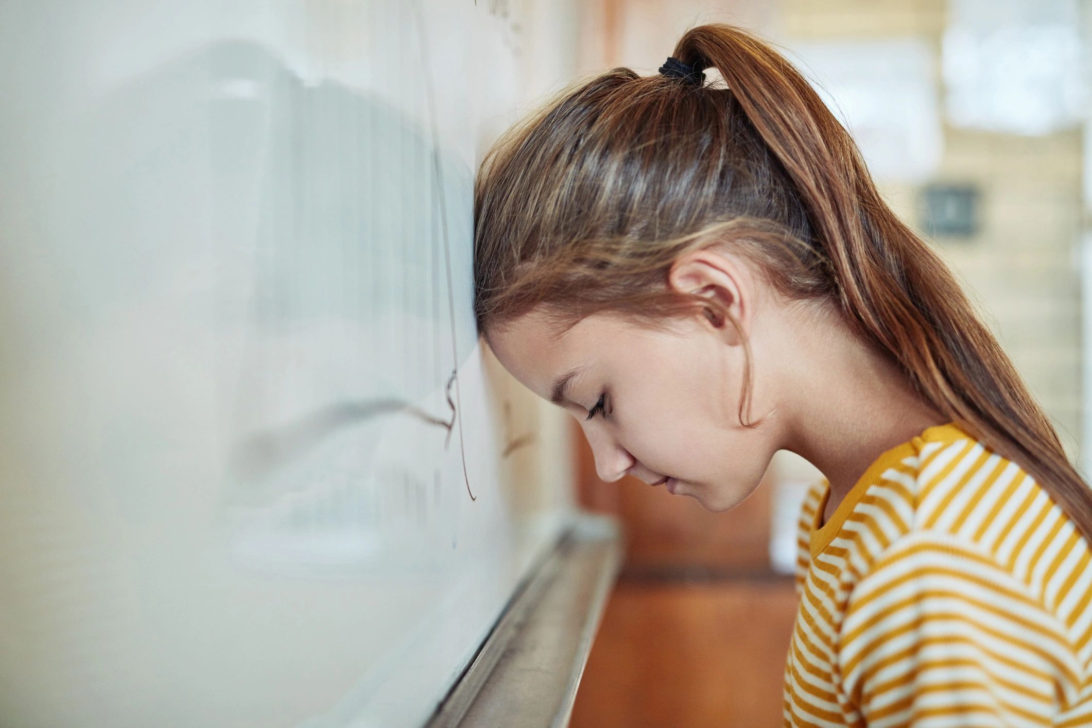 Young girl with head against a whiteboard, looking down.