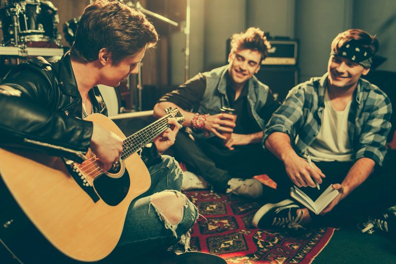 selective focus of musician playing acoustic guitar near happy friends sitting with crossed legs