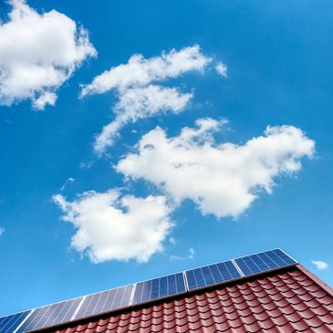 Solar panels installed on a red tiled roof under a bright blue sky.