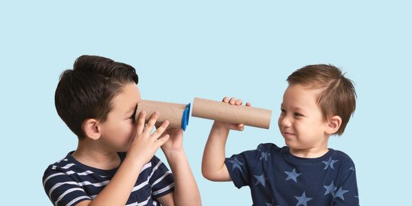 Two young boys play with cardboard tube telephones against a blue background.