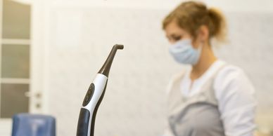 Dental curing light on charger with dentist in background.