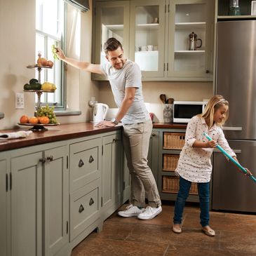 A man and a young girl cleaning a modern kitchen together.