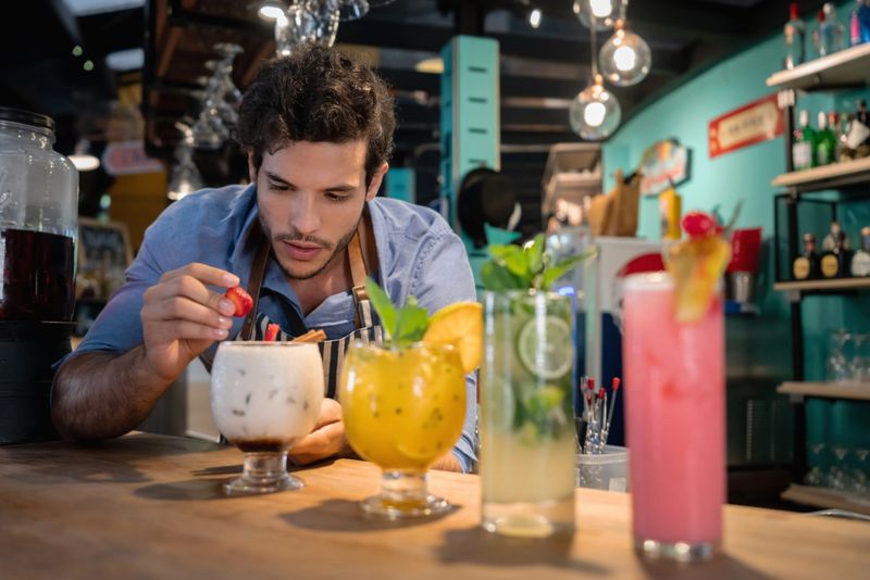 Bartender decorating beautiful cocktails at the bar with strawberries - food and drinks concepts