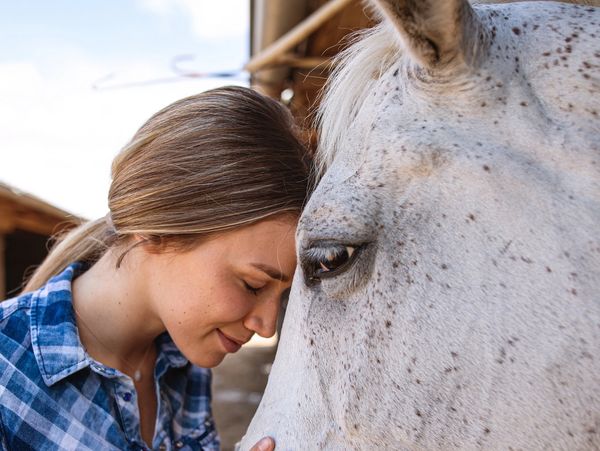 Woman gently resting her forehead against a white horse.