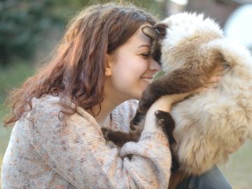 A woman lovingly nuzzles a fluffy cat outdoors.