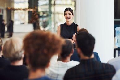 Woman speaking happily to an audience in a bright room.