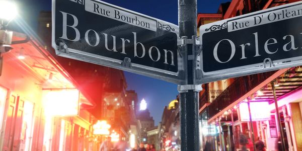 Street signs for Bourbon and Orleans streets at night in a lively city scene.