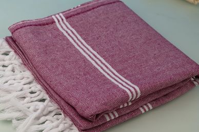 Folded maroon towel with white stripes and fringes.