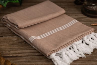 Folded beige towel with white stripes and fringes on wooden surface.