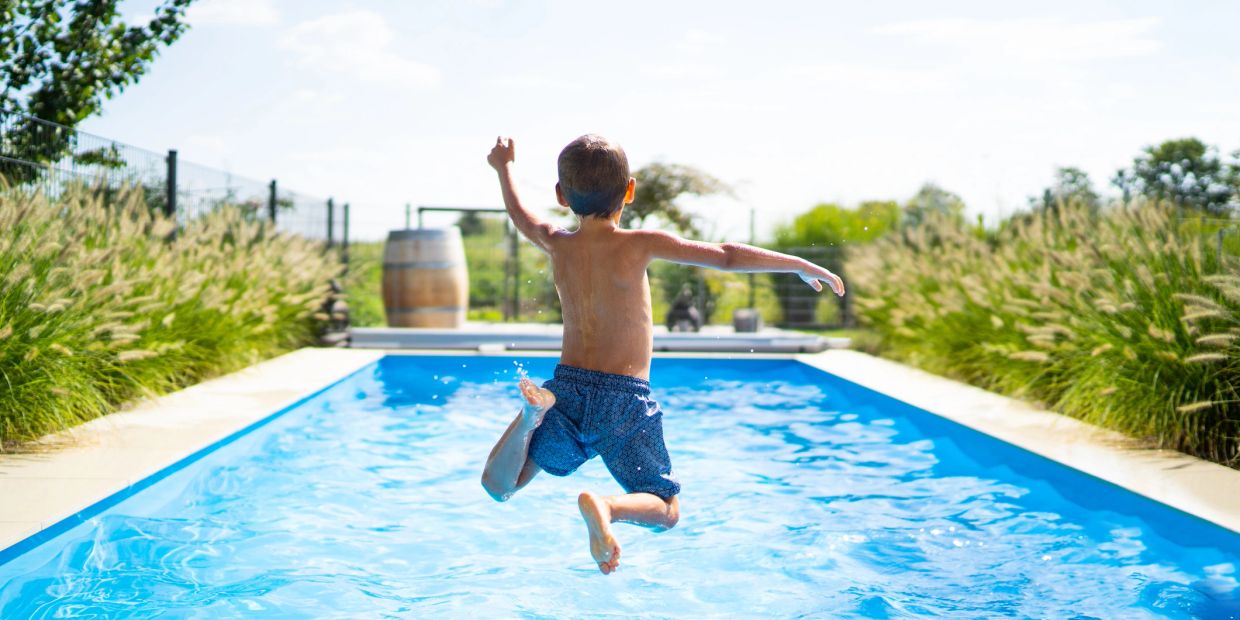 Child jumping into a pool on a sunny day.
