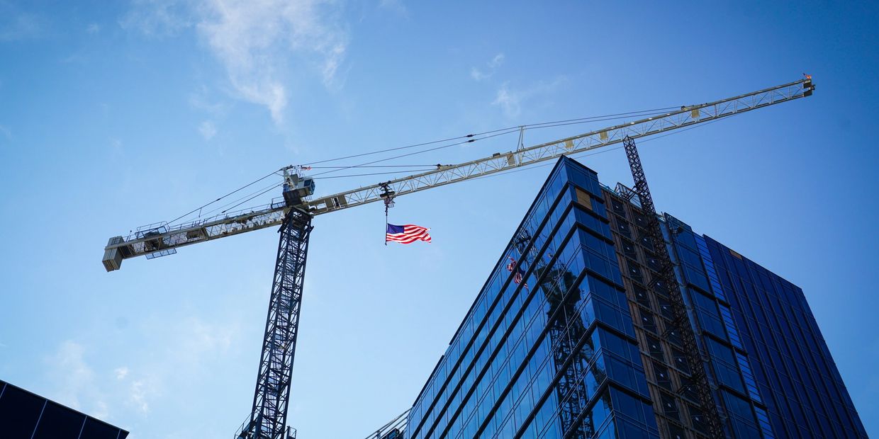A crane holding a waving American flag above a modern glass building under construction.