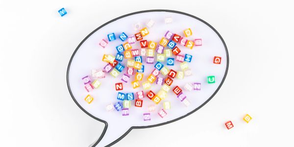 Speech bubble filled with colorful alphabet beads on a white background.