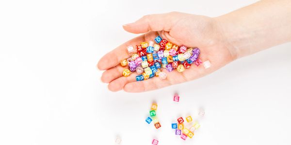 Hand holding colorful alphabet beads with some scattered on white surface.