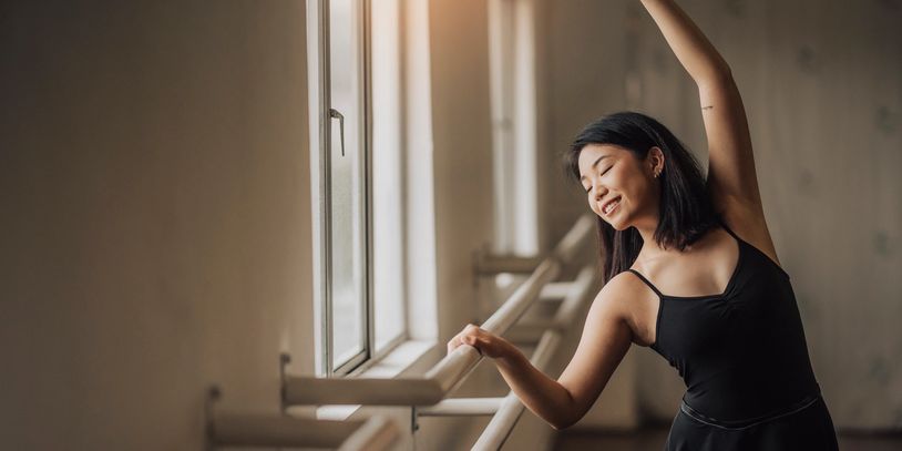 Woman practicing ballet by the window with a graceful smile.