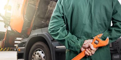 Mechanic holding a wrench behind back near an open truck hood.