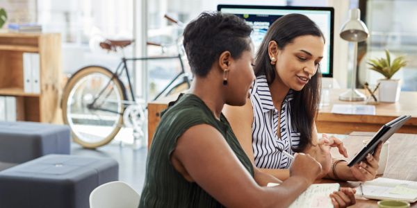 Two women collaborating over a tablet in a modern office space.