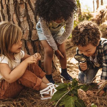Three children exploring nature with curiosity and a magnifying glass.
