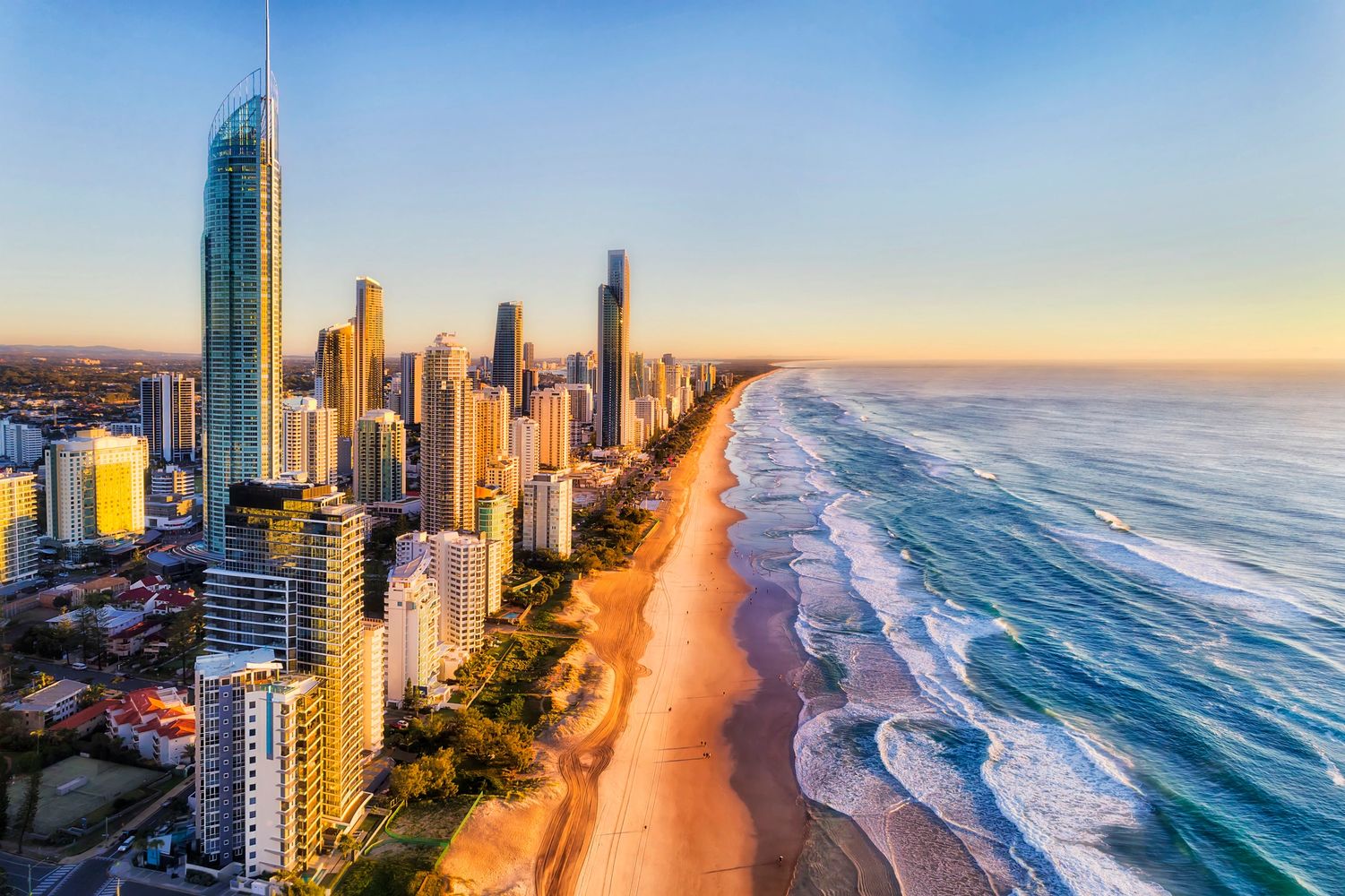 Sunlit city skyline beside a long sandy beach and blue ocean waves.
