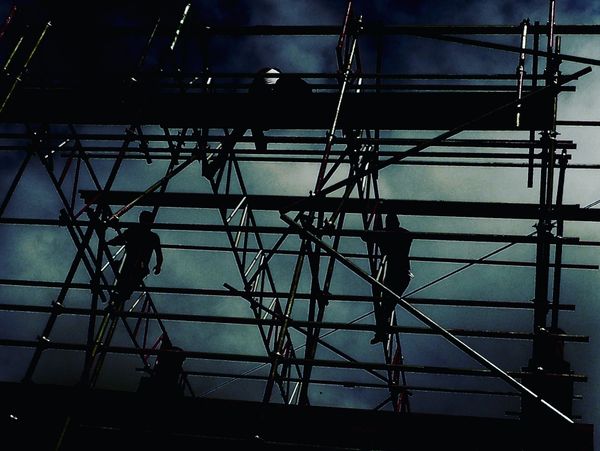 Silhouettes of workers on scaffolding against a dark, cloudy sky.
