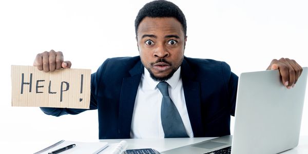 Man in suit holding a 'HELP!' sign at his desk.