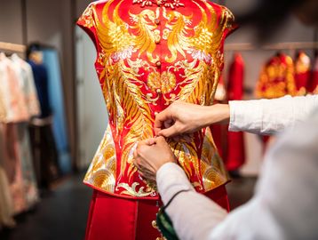 Person adjusting an ornate traditional garment on a mannequin.