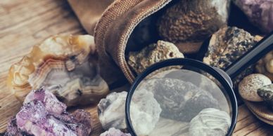 A magnifying glass examines various colorful mineral and rock samples.