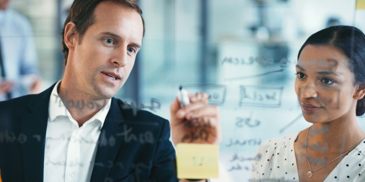Two professionals collaborating and brainstorming ideas on a transparent board.