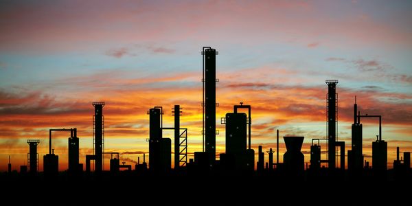 Silhouette of an industrial refinery against a colorful sunset sky.
