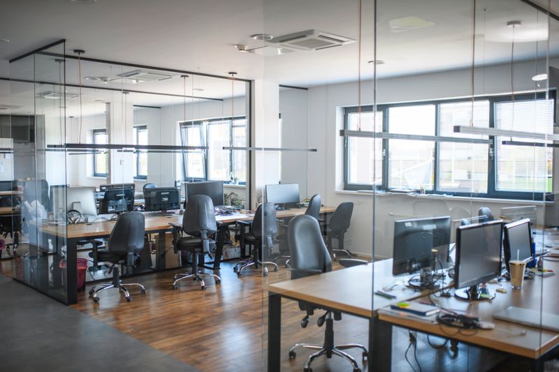 General view of modern open plan office space with glass see-through partitions and extended workstations.