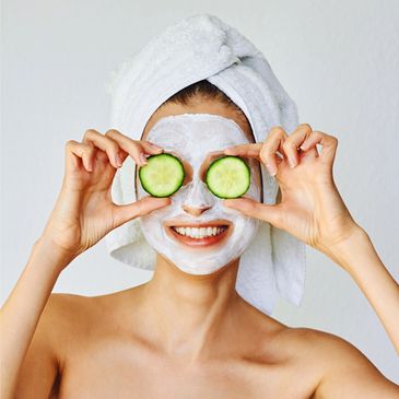 Woman with facial mask and cucumber slices on eyes, wrapped in towel.