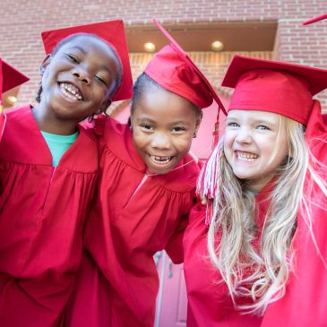 Three kids in red graduation gowns smiling.
