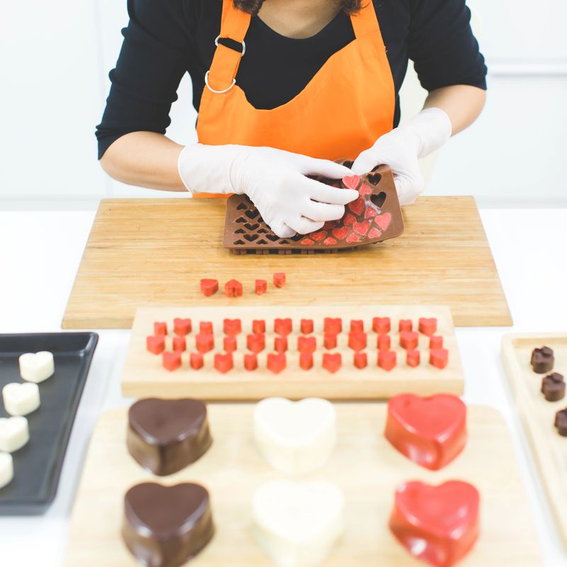 Chef in orange apron putting and arranging finished heart shape chocolate in to tray ready to sell in chocolate shop.