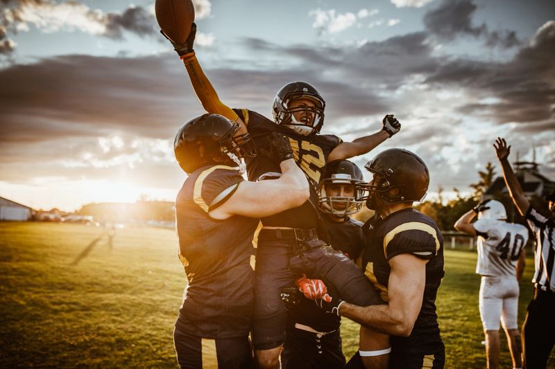 Team of American football players celebrating victory at sunset.