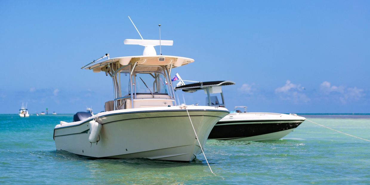 Two boats anchored in clear, calm ocean water under a bright blue sky.
