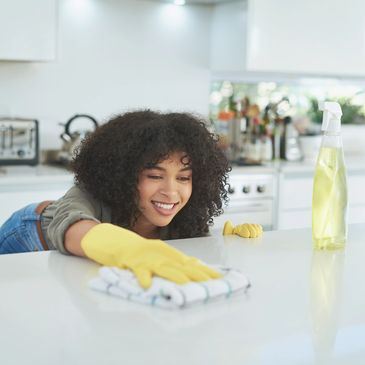 A woman with curly hair wearing yellow gloves cleaning a kitchen counter.