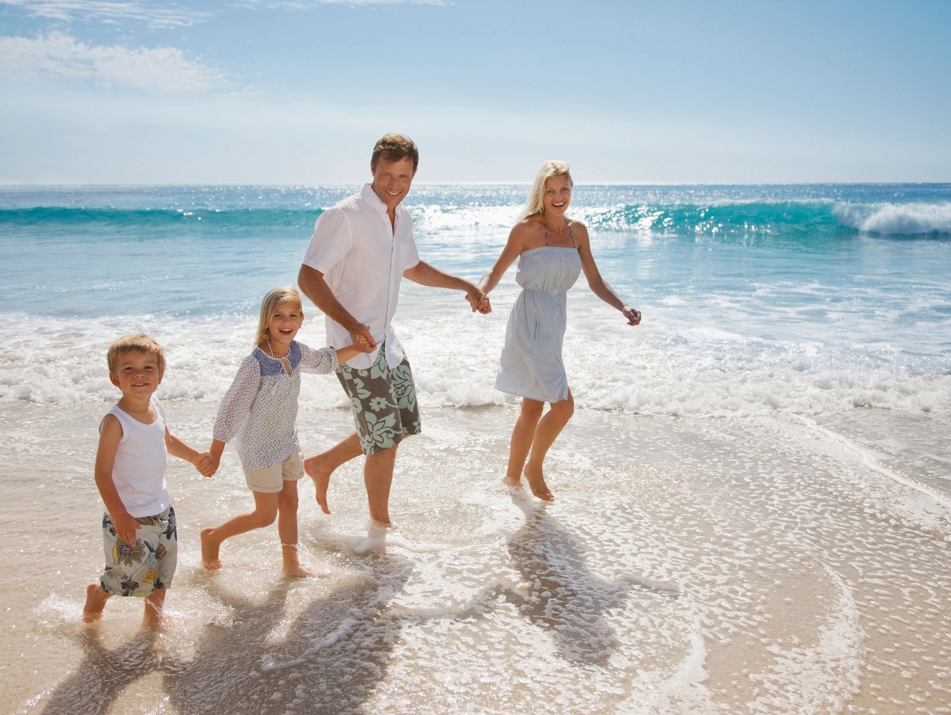 Happy family holding hands and walking along the beach shore with waves.