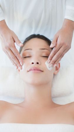 A woman receiving a gentle facial treatment with cream application.