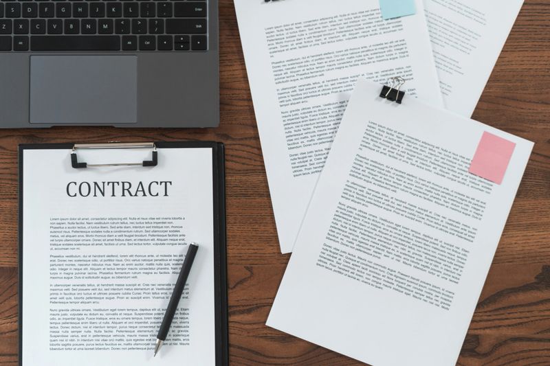 Top view of contract in clipboard lying at office on wooden table with laptop and documents