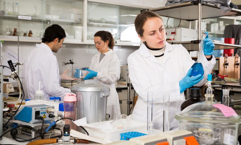 Professional female chemist working in laboratory, analyzing liquid samples in test flasks