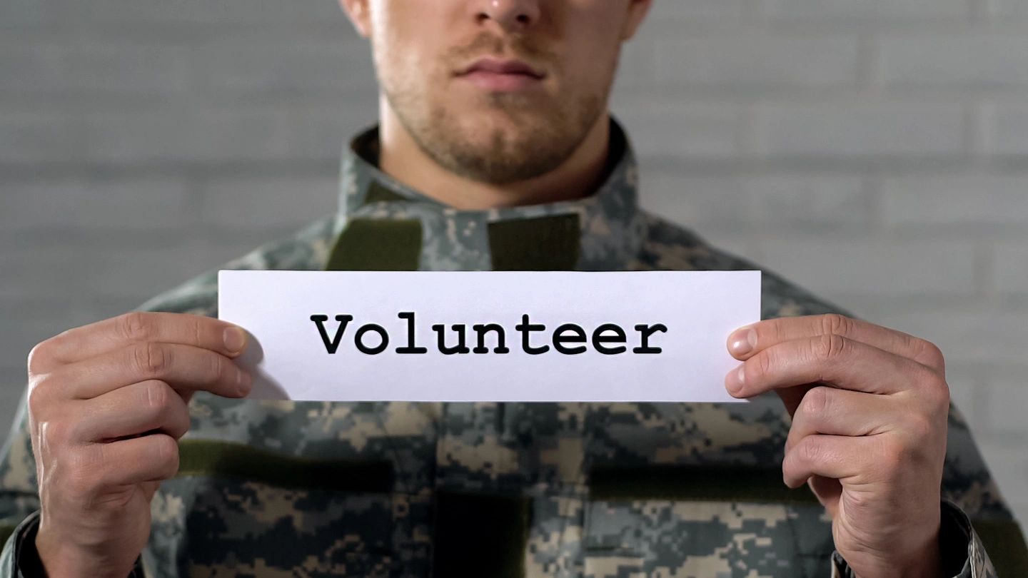 A soldier holds a sign that says 'Volunteer'.